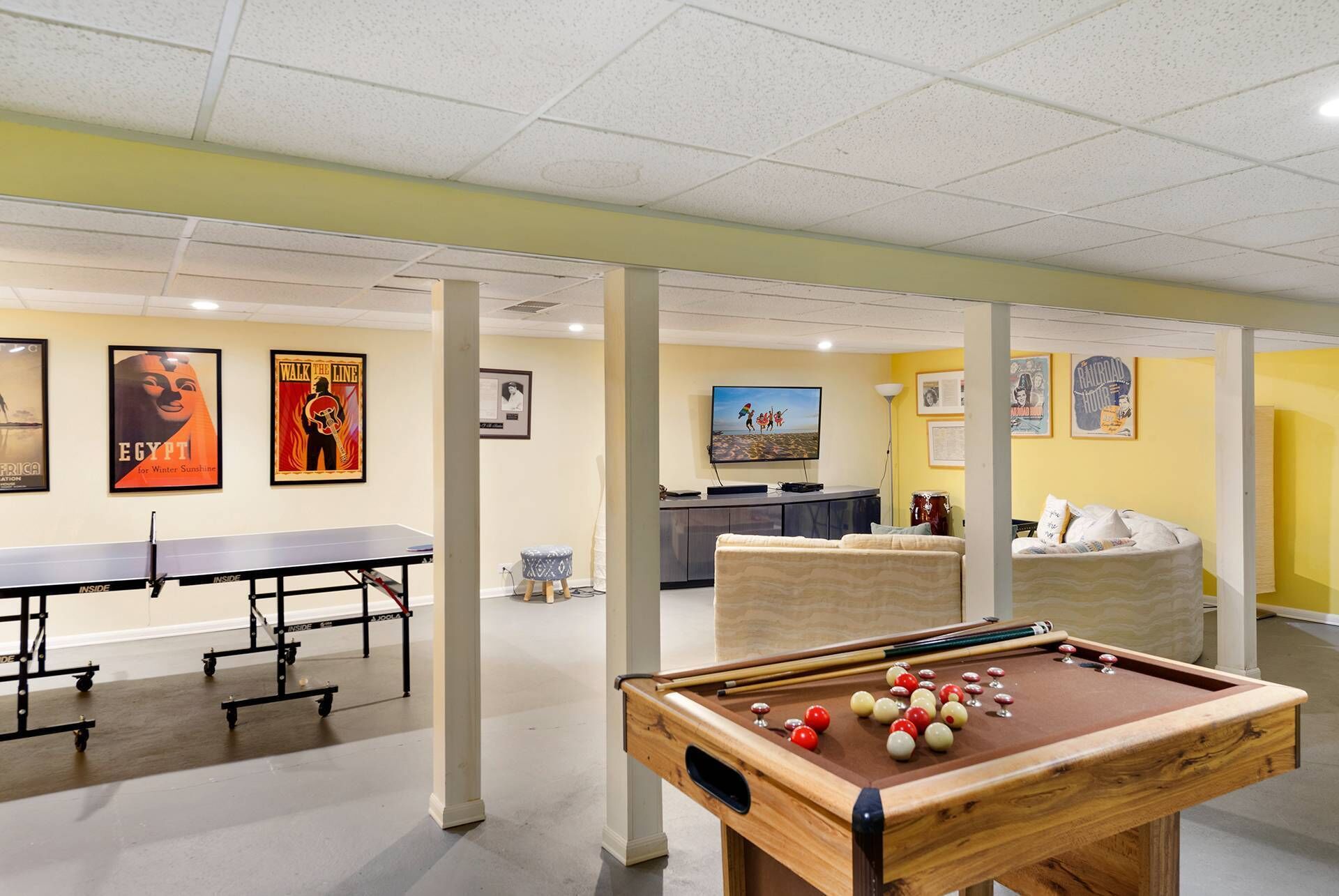 A pool table with balls, a ping pong table, and a sofa in a room with yellow walls and ceiling.