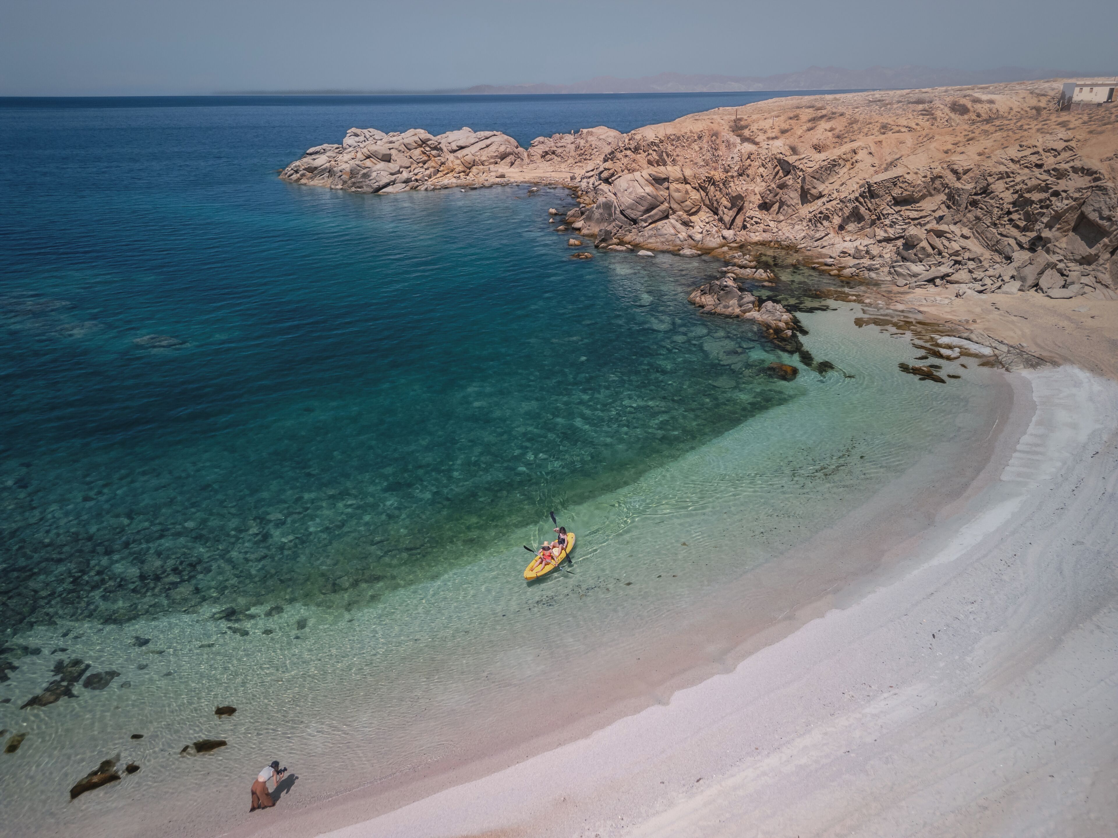 A coastal landscape with clear waters, rocky outcrops, and a sandy beach.