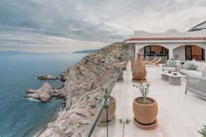 Ein Küstenanwesen mit Terrasse und Meerblick, ausgestattet mit Gartenmöbeln und Blumentöpfen.