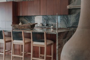 Eine moderne Küche mit Marmorarbeitsplatte, Holzbarhocker und einer integrierten Spüle.