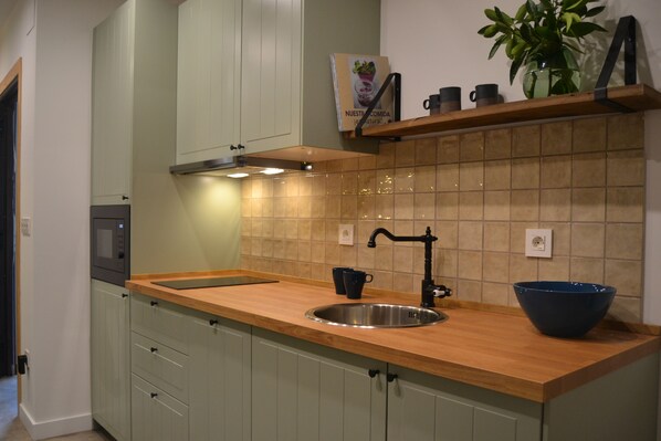 Una cocina con encimera de madera, pileta de acero inoxidable y grifo negro.