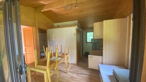 Interior em madeira com área de refeições, pequena cozinha e porta que dá para outro cômodo.