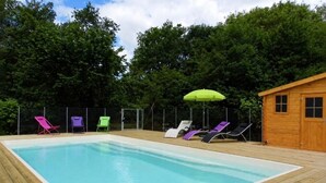 Piscina retangular com deck de madeira, rodeada por espreguiçadeiras e um chalé de madeira.