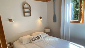 A bedroom with a wooden ceiling, a bed with white bedding, a wall-mounted mirror, and a window with curtains.