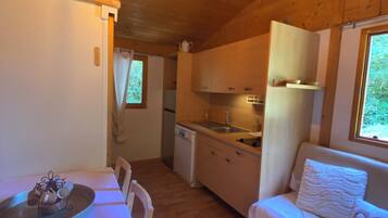 A compact cabin interior with a dining table, a sofa, a kitchenette, and a small bathroom.