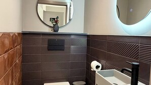 A modern bathroom with a toilet, sink, and mirror. - Uno by the Sea (St Ives)