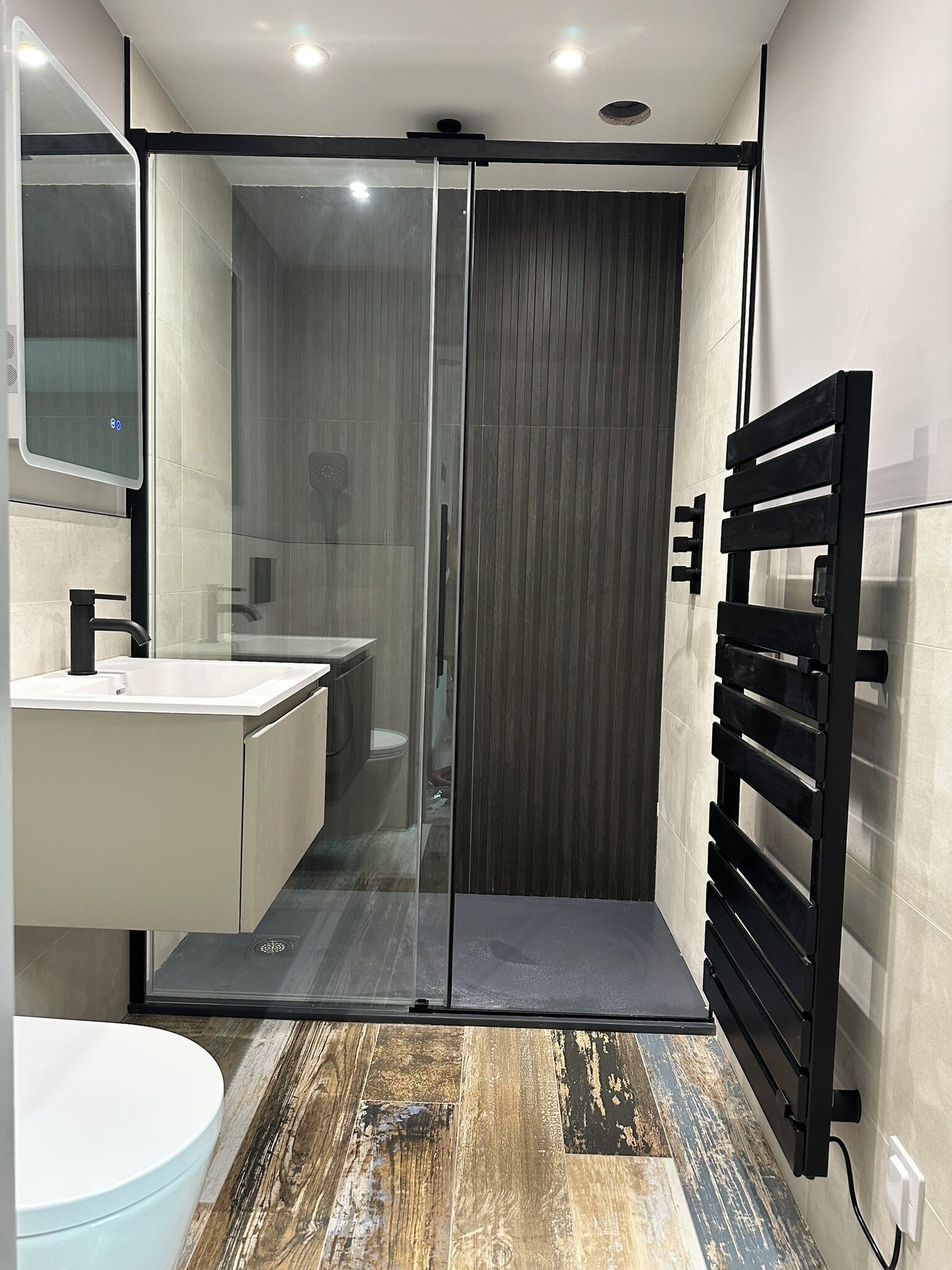 A modern bathroom with a glass shower enclosure, a black towel rack, and a white sink.
