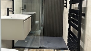 A modern bathroom with a glass shower enclosure, a black towel rack, and a white sink. - Uno by the Sea (St Ives)