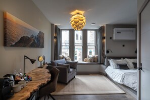 A modern bedroom with a bed, a sofa, a desk with a lamp, and a large window. - Uno by the Sea (St Ives)