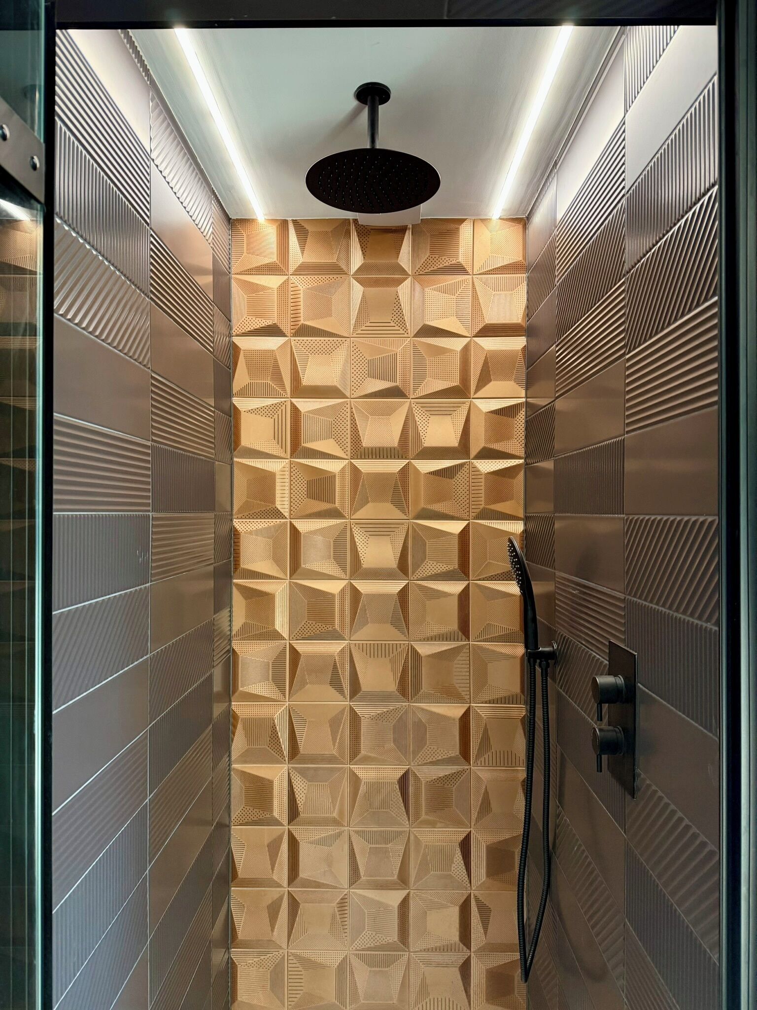 A modern shower with geometric patterned tiles, a black handheld showerhead, and a handheld shower hose.
