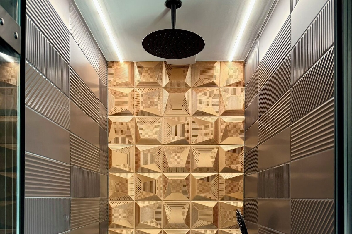 A modern shower with geometric patterned tiles, a black handheld showerhead, and a handheld shower hose.