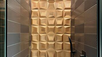 A modern shower with geometric patterned tiles, a black handheld showerhead, and a handheld shower hose.