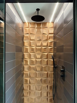 A modern shower with geometric patterned tiles, a black handheld showerhead, and a handheld shower hose. - Uno by the Sea (St Ives)
