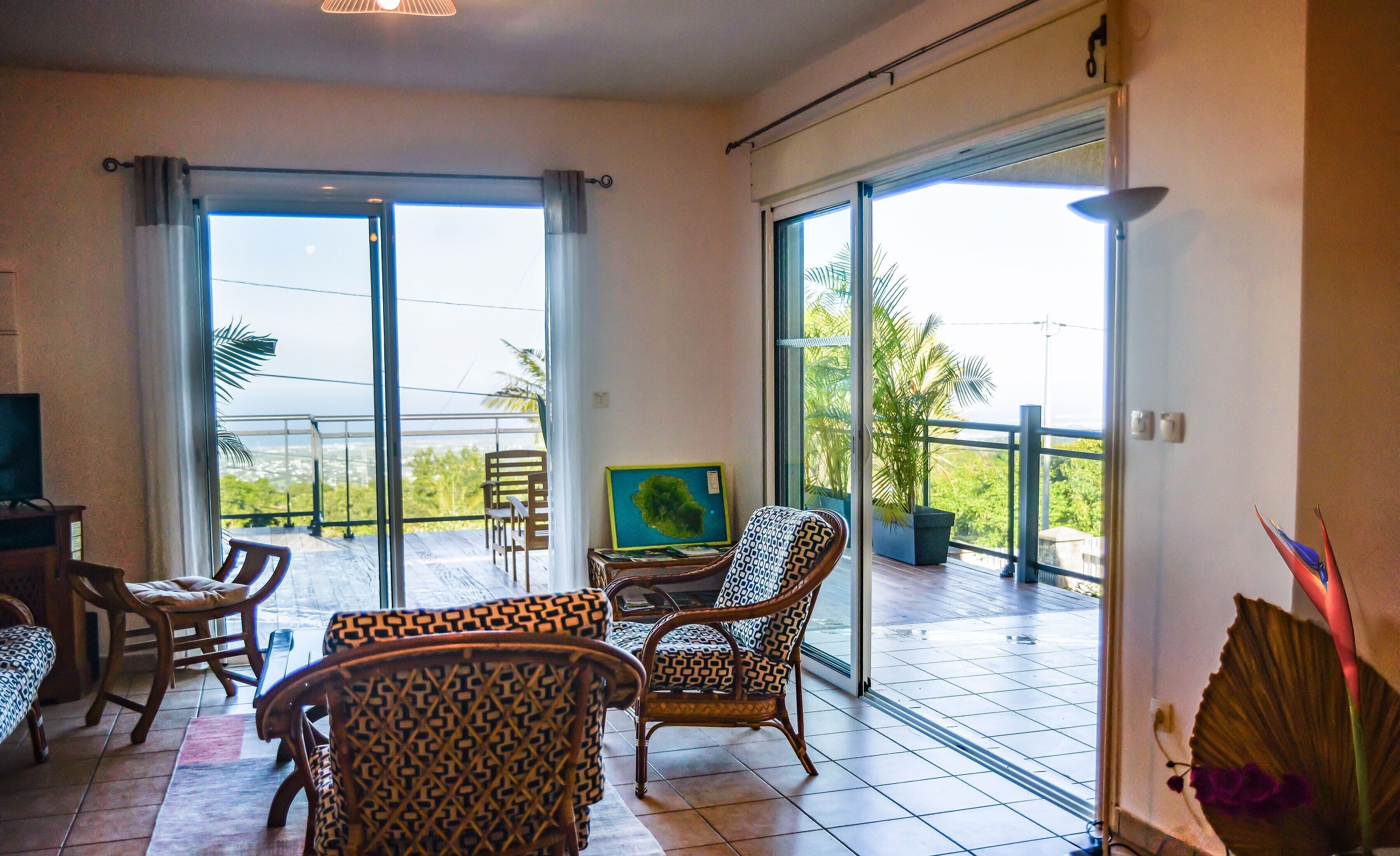 Habitación amplia con balcón, amoblada con sillas y una mesa, y ventanas grandes que ofrecen vistas al exterior.