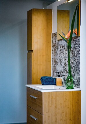 A modern bathroom with a wooden cabinet, a sink, and a decorative plant. - Ty Lodge Réunion – Pool, Spa, Ocean View, Garden, Near Saint-Pierre & Volcano (Le Tampon)