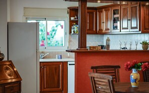 A kitchen with wooden cabinets, a refrigerator, a dining table with chairs, and a vase with flowers. - Ty Lodge Réunion – Pool, Spa, Ocean View, Garden, Near Saint-Pierre & Volcano (Le Tampon)