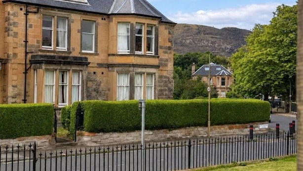 A two-story stone building with a pitched roof, multiple windows, and a well-maintained hedge in front. - Large Flat in Edinburgh 4/1 (Edinburgh)