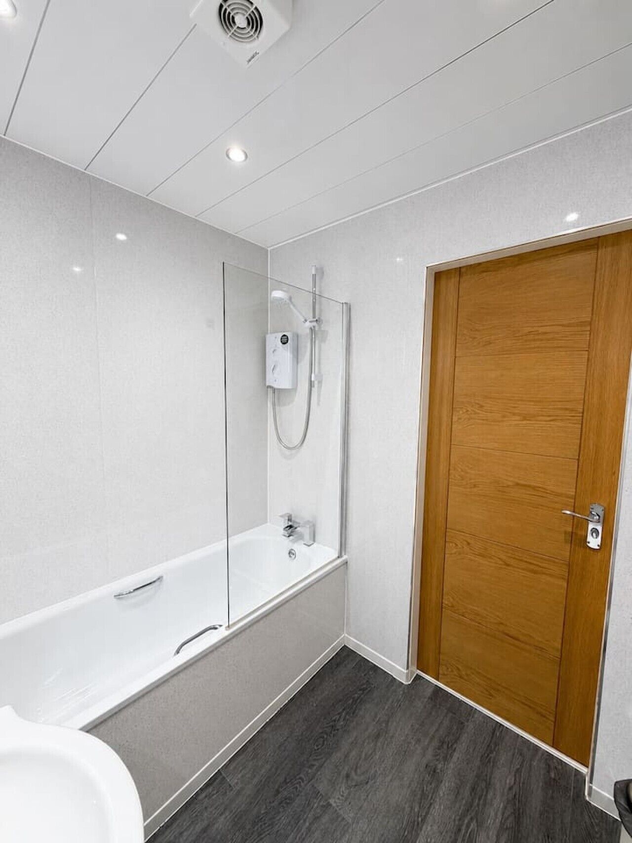 A modern bathroom with a glass-enclosed shower, a white bathtub, and a wooden door.