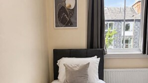 A neatly made bed with a beige quilt and pillows, a rolled towel, and a framed artwork on the wall. - Large Flat in Edinburgh 4/1 (Edinburgh)