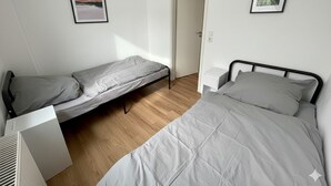 A bedroom with two beds, a white radiator, and framed pictures on the wall. - HomeBase with a kitchen and 5 single beds, centrally located (Krefeld)