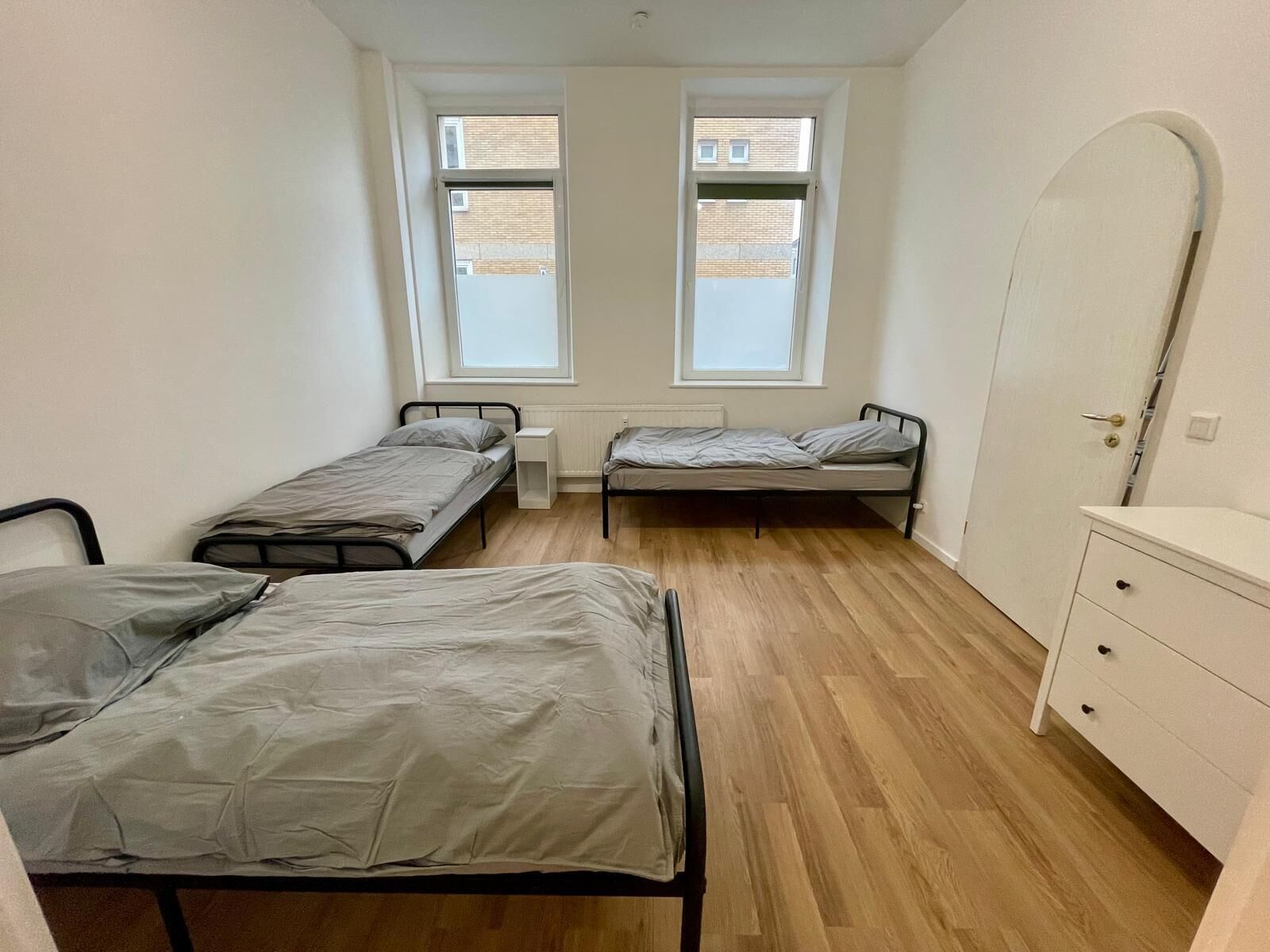 Een kleine, nette kamer met twee eenpersoonsbedden, een witte dressoir en twee ramen.