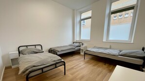 A room with two single beds, a white desk, and a window with a view of a brick building. - HomeBase with a kitchen and 5 single beds, centrally located (Krefeld)