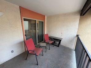 A balcony with two red chairs and a table, a sliding glass door, and a textured wall. - NEW Desert Gem | Spacious 2BR Tucson Getaway (Tucson)