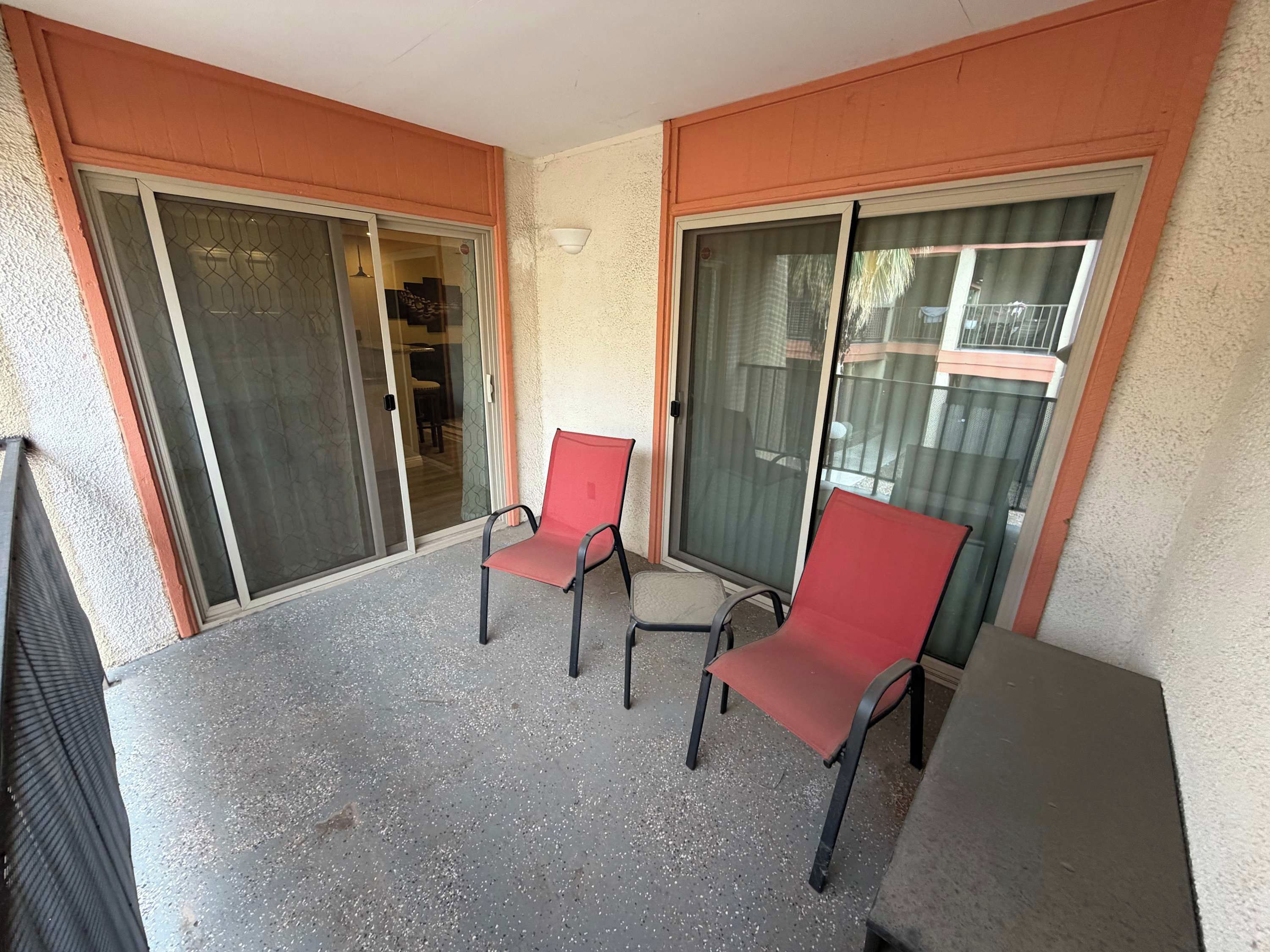 Un balcon avec deux chaises et une table, des portes vitrées et un mur à texture.