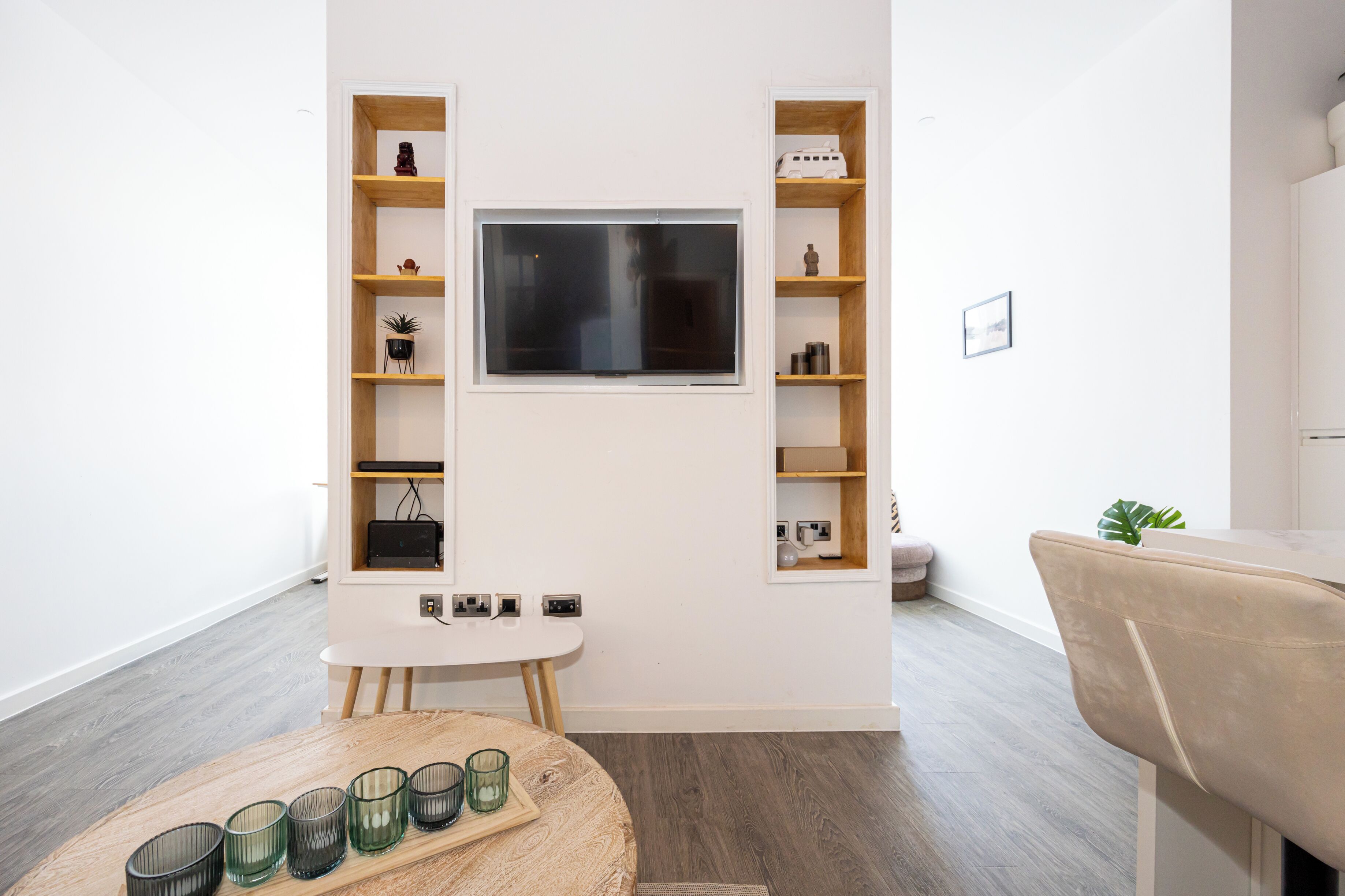 A modern living room with a flat-screen TV mounted on the wall, surrounded by wooden shelving units.