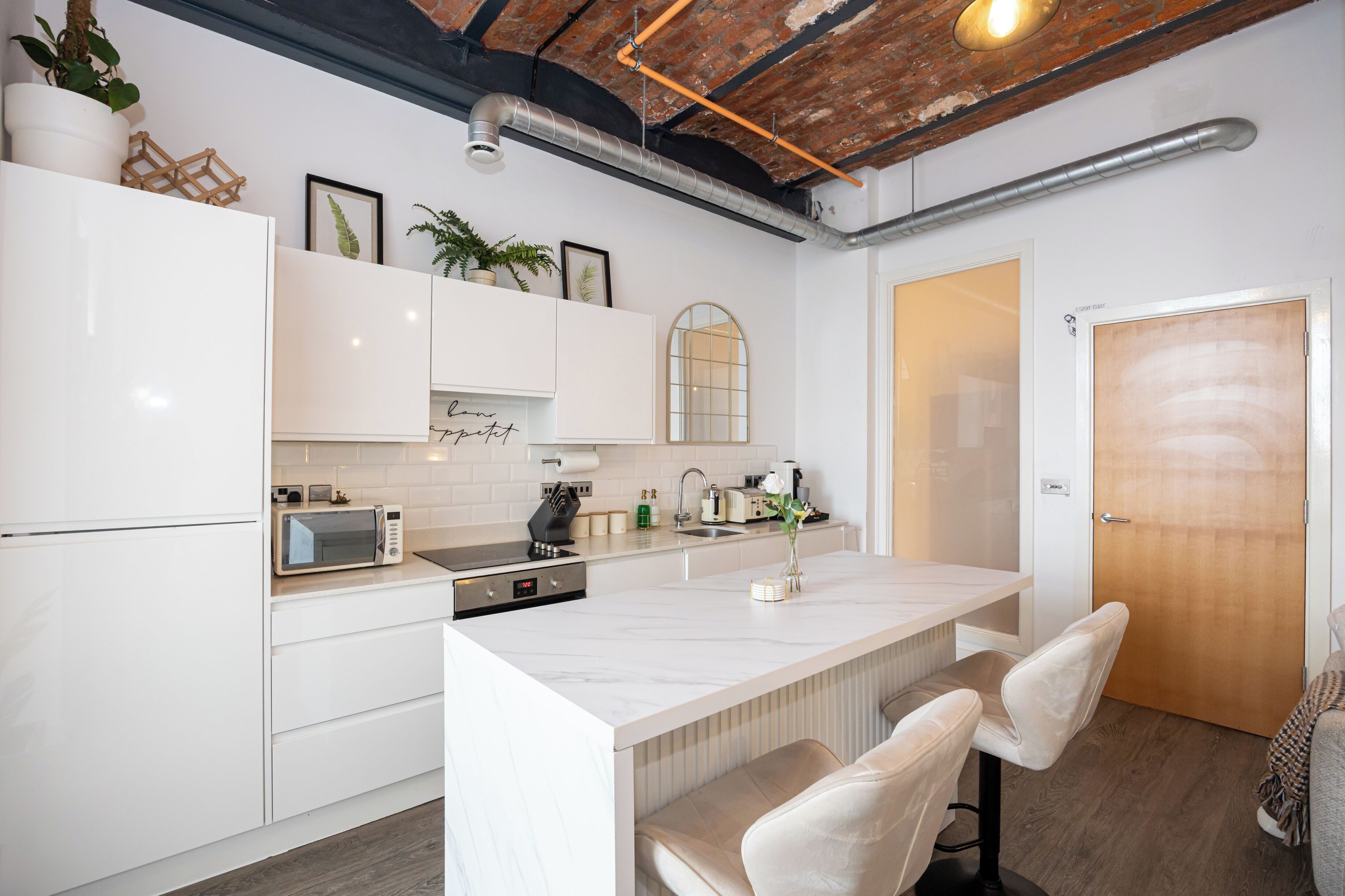 A modern kitchen with white cabinetry, a built-in microwave, a coffee maker, and a small island with seating.