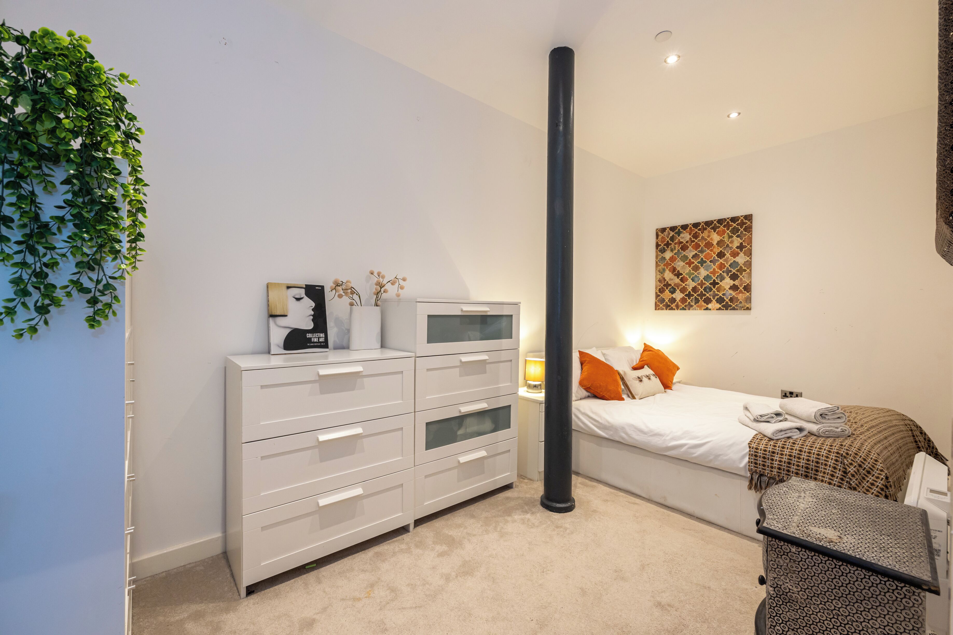 A bedroom with a bed, a dresser, a lamp, and a wall-mounted artwork.