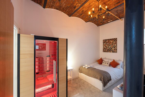 A bedroom with a bed, a red-lit storage unit, a chandelier, and a patterned wall decoration.