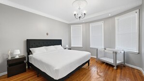 Une chambre à coucher avec un grand lit, des tables de chevet, une commode, un lustre et un berceau.