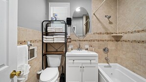 Ein kleines Badezimmer mit Toilette, Waschbecken und Badewanne. Ein Regal mit Handtüchern und Pflegeprodukten ist vorhanden.