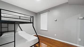 A single bunk bed in a room with wooden flooring and a window with blinds.