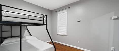 Una cama individual en literas en una habitación con piso de madera y una ventana con persianas.