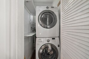 A laundry room with two stacked washers and dryers, a metal rack, and a white wall. - Spacious 24-Bed Home Near NYC & Newark Airport – Perfect for Groups! (Bayonne)