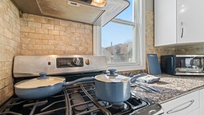 Uma cozinha com fogão a gás, duas panelas, micro-ondas e janela com vista para edifícios.