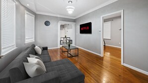 Uma sala de estar moderna com um sofá cinzento, uma mesa de centro e uma TV fixada na parede.