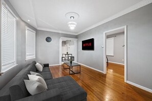En moderne stue med en grå sofa, et sofabord og et fjernsyn ophængt på væggen.