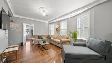 Una sala de estar con un sofá seccional color crema, un sofá gris, una mesa de centro de madera y un banco de madera.