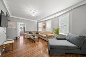 Una sala de estar con un sofá seccional color crema, un sofá gris, una mesa de centro de madera y un banco de madera.