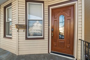 A house with a front door, a mailbox, and a window with a view of a building. - Spacious 24-Bed Home Near NYC & Newark Airport – Perfect for Groups! (Bayonne)