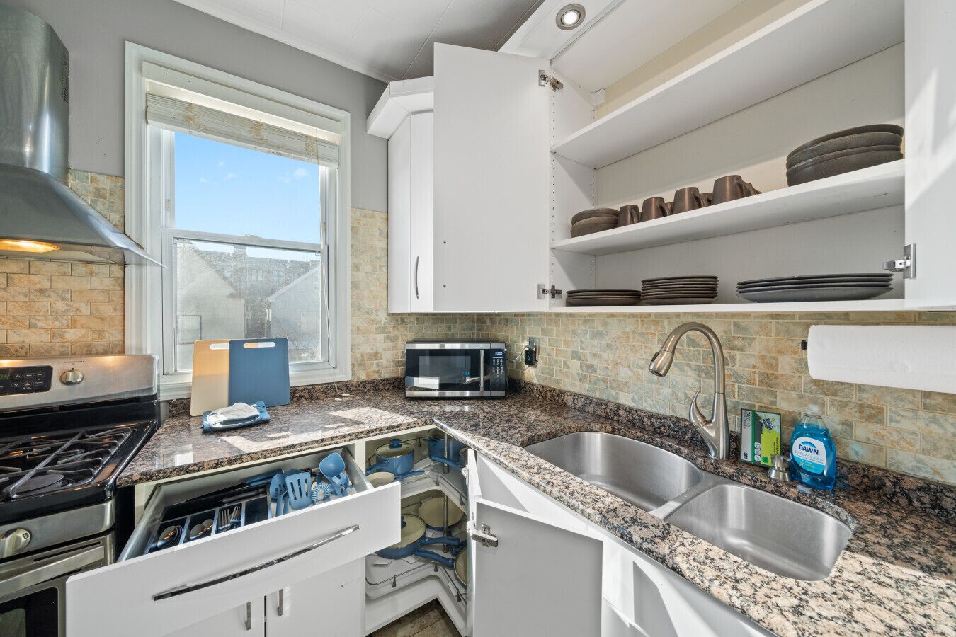 Una cocina con estufa de acero inoxidable, microondas, pileta y ventana con vista.
