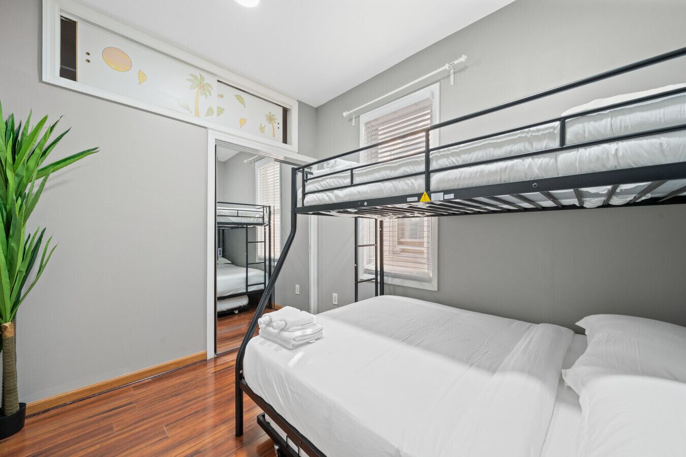 A bunk bed room with a wooden floor, a potted plant, and a door leading to another room.