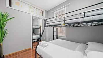 A bunk bed room with a wooden floor, a potted plant, and a door leading to another room.