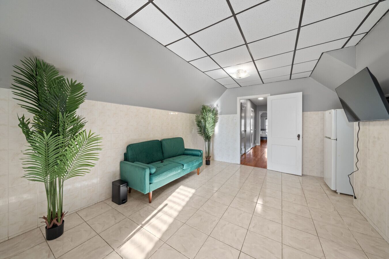 A spacious living area with a teal sofa, potted plants, and a tiled floor.
