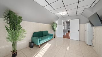 A spacious living area with a teal sofa, potted plants, and a tiled floor.