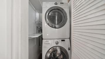A laundry room with two stacked washers and dryers, a metal rack, and a white wall.