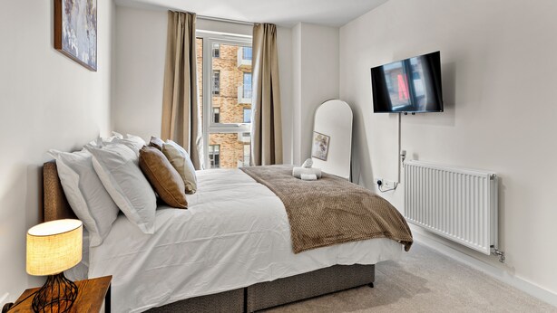 Ein Schlafzimmer mit einem Bett, einem Fernseher, einem Heizkörper und einem Fenster mit Vorhängen.